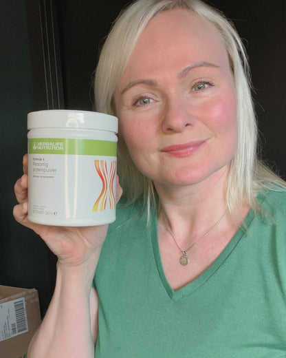 En boks Herbalife Formula 3 Personlig proteinpulver og Helga som viser den frem.