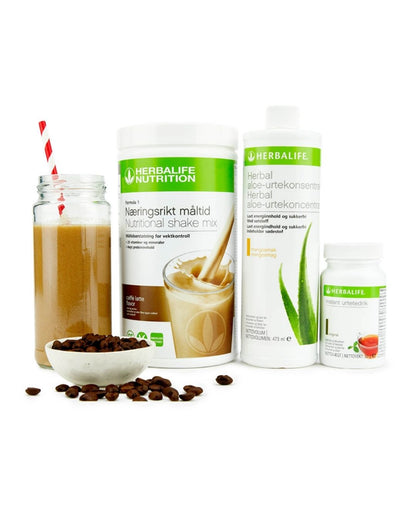 Bildet viser Herbalife-produktene som Frokostpakke basic caffe latte består av; Herbalife-shake med kaffelattesmak, Herbal Aloe aloevera-juice med mangosmak og Instant urtete med original-smak samt en kaffe latte-shake i et glass med sugerør og noen kaffebønner i en skål.