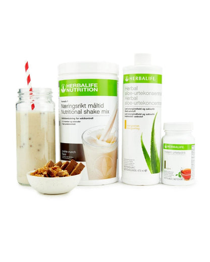 Bildet viser Herbalife-produktene som Frokostpakke basic cookie crunch består av; Herbalife-shake med cookiecrunch-smak, Herbal Aloe aloevera-juice med mangosmak og Instant urtete med original-smak samt en Herbalife-shake i et glass med sugerør og noen cookies i en skål.
