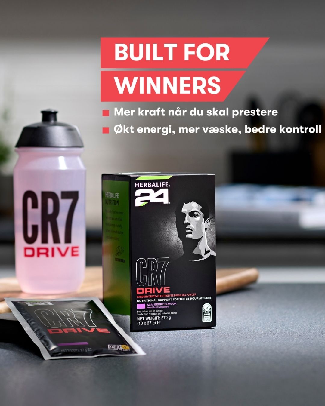 En pakke Herbalife H24 CR7 Drive, en løs porsjonspose og en drikkeflaske med sportsdrikk. På bildet står teksten “Built for winners. Mer kraft når du skal prestere. Økt energi, mer væske, bedre kontroll”. 