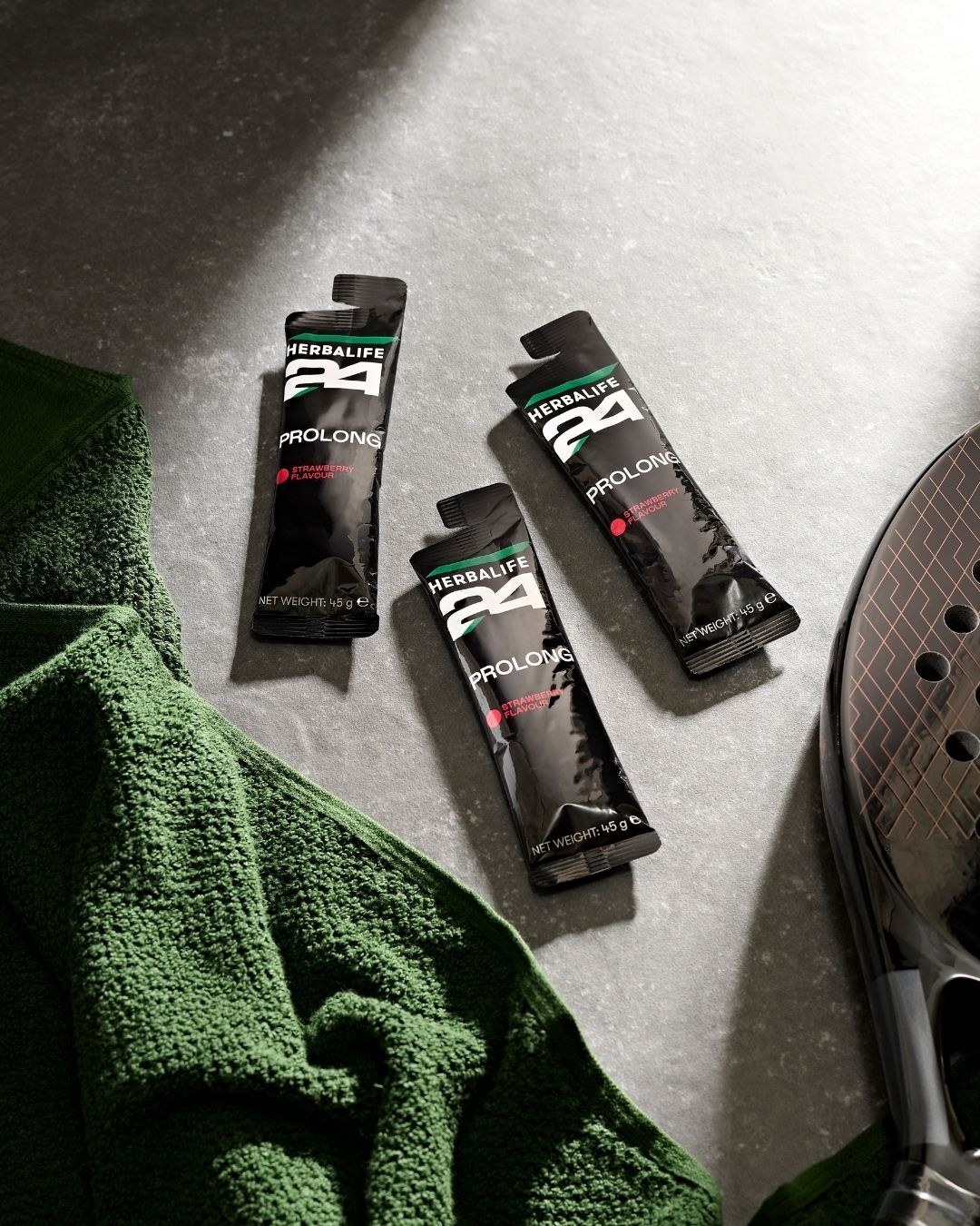 Tre porsjonsposer Herbalife H24 Prolong Energy Gel, et håndkle og en racket.