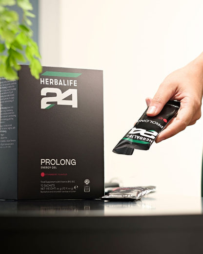 En pakke Herbalife H24 Prolong Energy Gel på et bord og en person som tar en porsjonspose i hånden. 