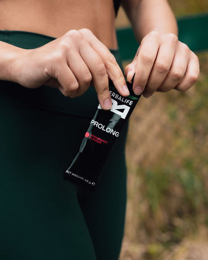 En kvinne i treningsøy som åpner en porsjonspose Herbalife H24 Prolong Energy Gel. 
