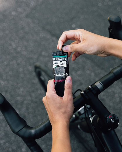 En person på sykkel holder en pose Herbalife H24 Prolong Energy Gel i hånda.