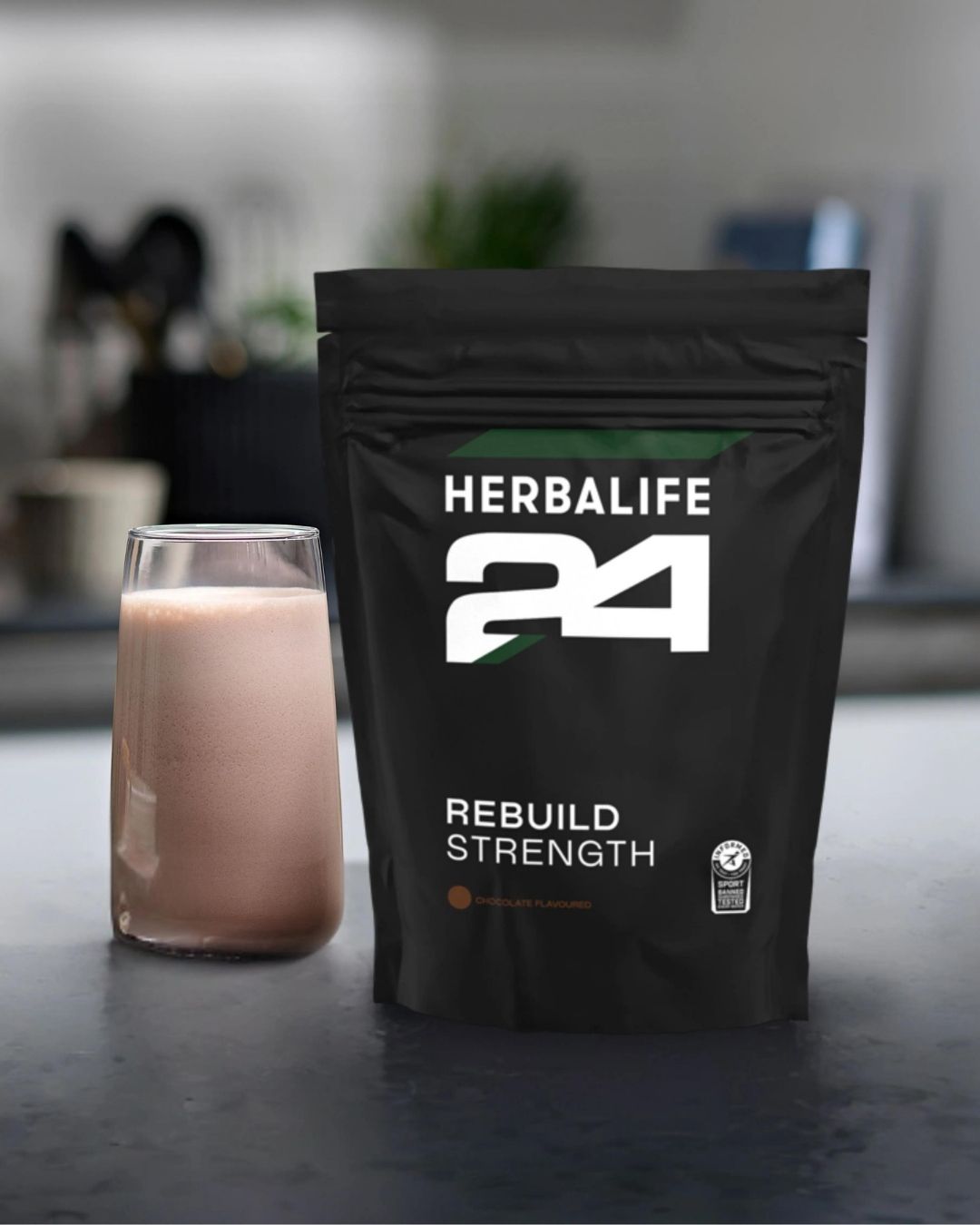 H24 Rebuild Strength pose med et glass proteinshake på en kjøkkenbenk. 