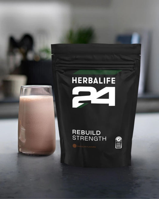 H24 Rebuild Strength pose med et glass proteinshake på en kjøkkenbenk. 