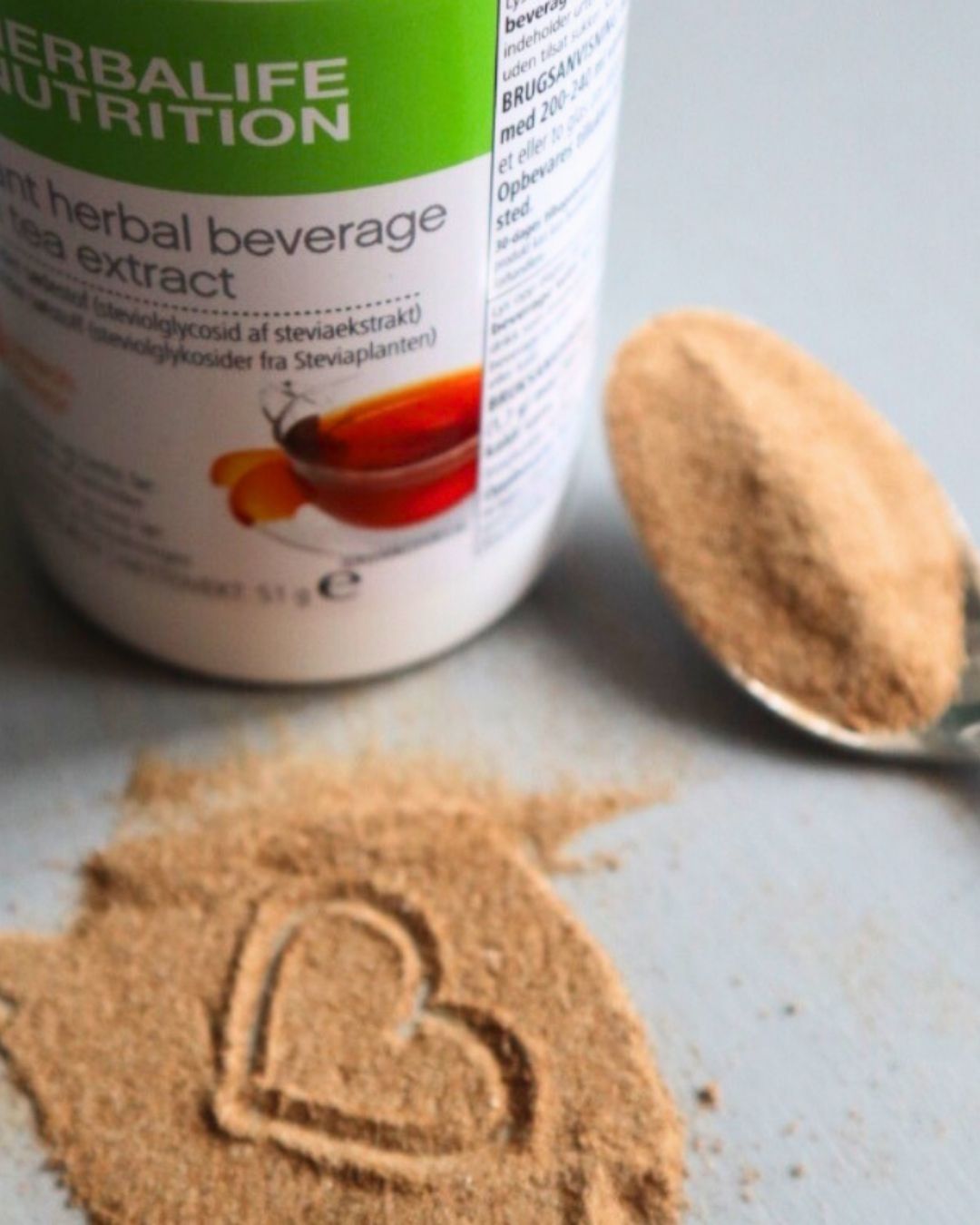 Herbalife instant urtete med skje og tepulver formet som et hjerte - energigivende drikk med naturlig smak og ekstrakt fra grønn te og stevia.