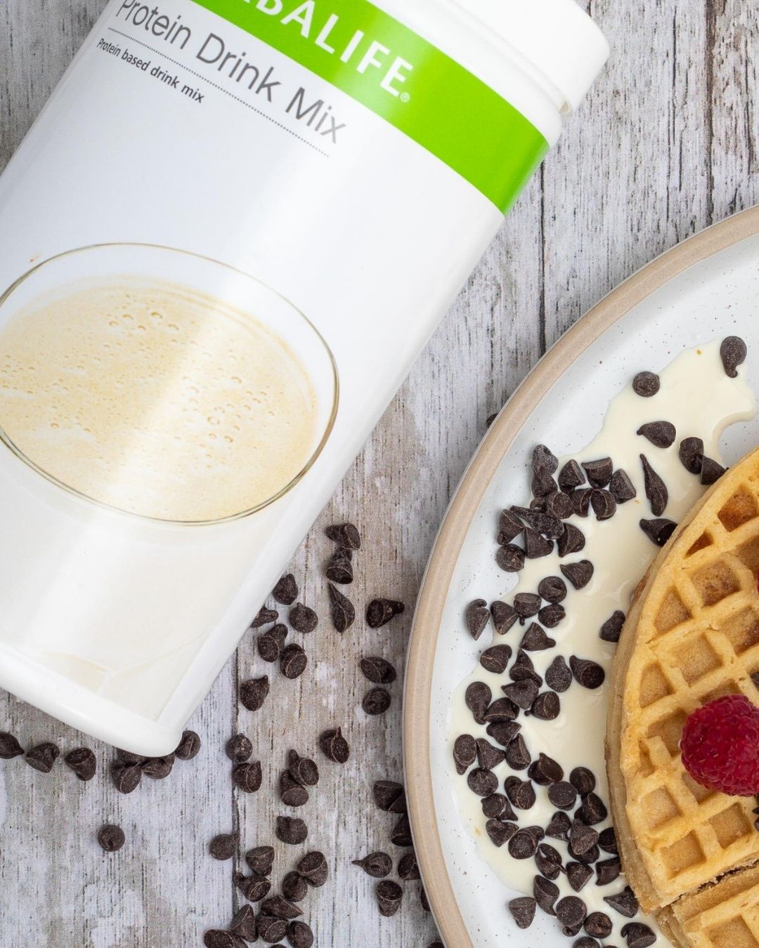 En boks Herbalife Protein Drink Mix liggende på et bord sammen med en tallerken med en belgisk vaffel med bringebær, jordbær og sjokoladestrøssel.
