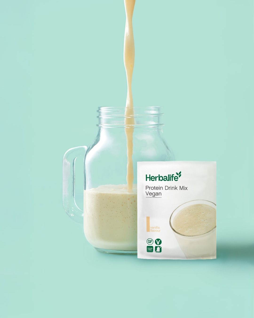 Herbalife Protein Drink Mix PDM Vegan vanilje porsjonspose med ferdig proteindrikk som helles i ei mugge.