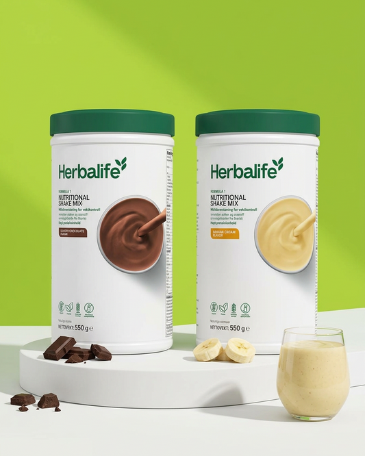 2 bokser Herbalife-shake med sjokolade og banansmak, på et hvitt display og en lysegrønn bakgrunn. Sjokolade- og bananbiter i forkant og et glass smoothie. 