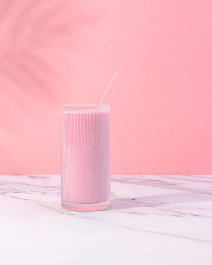 En rosa Herbalife-smoothie i et glass står på et marmorbord. Rosa vegg bak og det ses en skygge av et palmeblad på veggen.