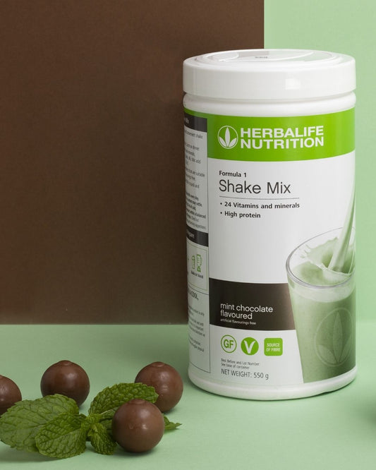 En boks Herbalife Formula 1 shakemix med Mint chocolate-smak og noen sjokoladekuler sammen med mintblader.