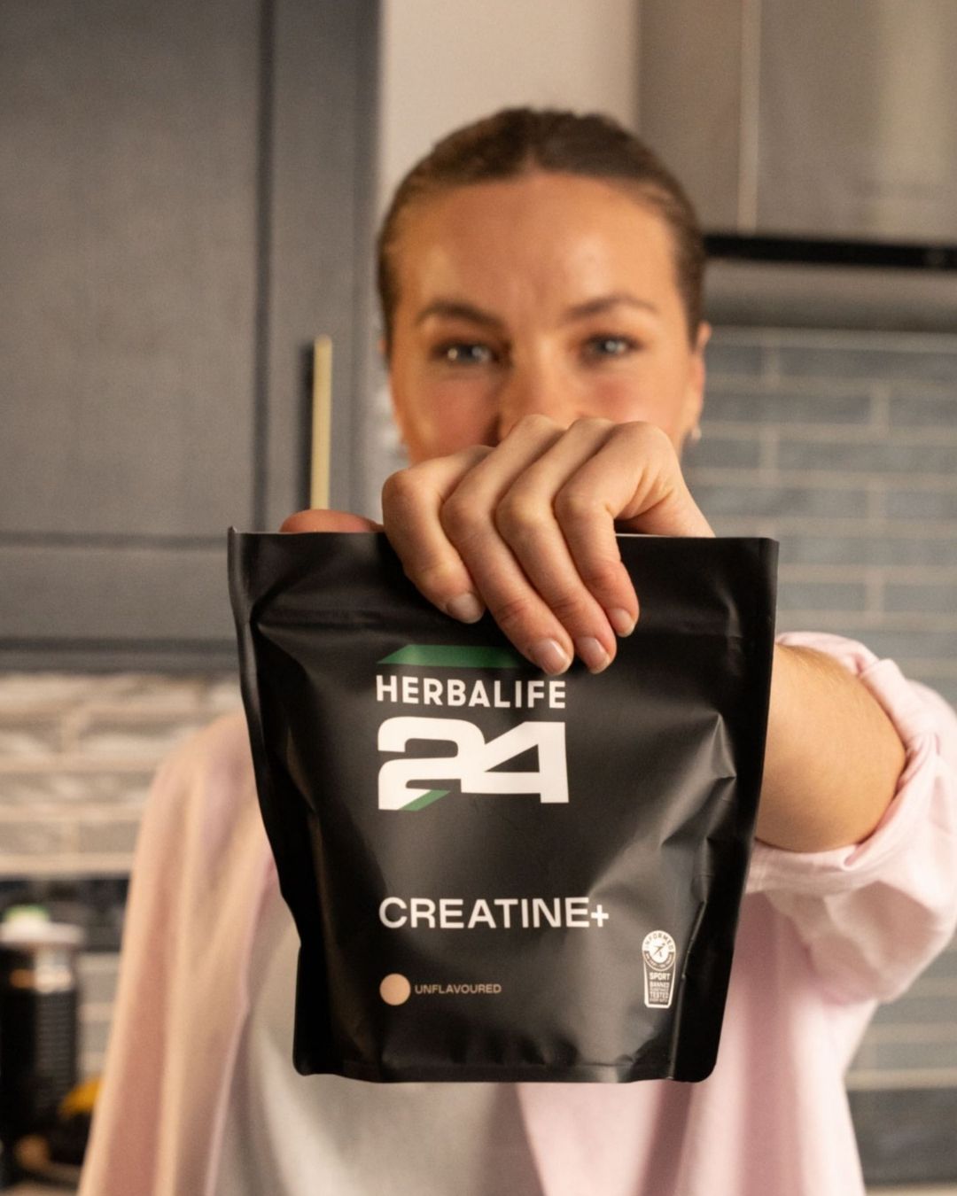 Kvinne på et kjøkken som holder frem en pose Herbalife H24 Creatine+ kreatin monohydrat