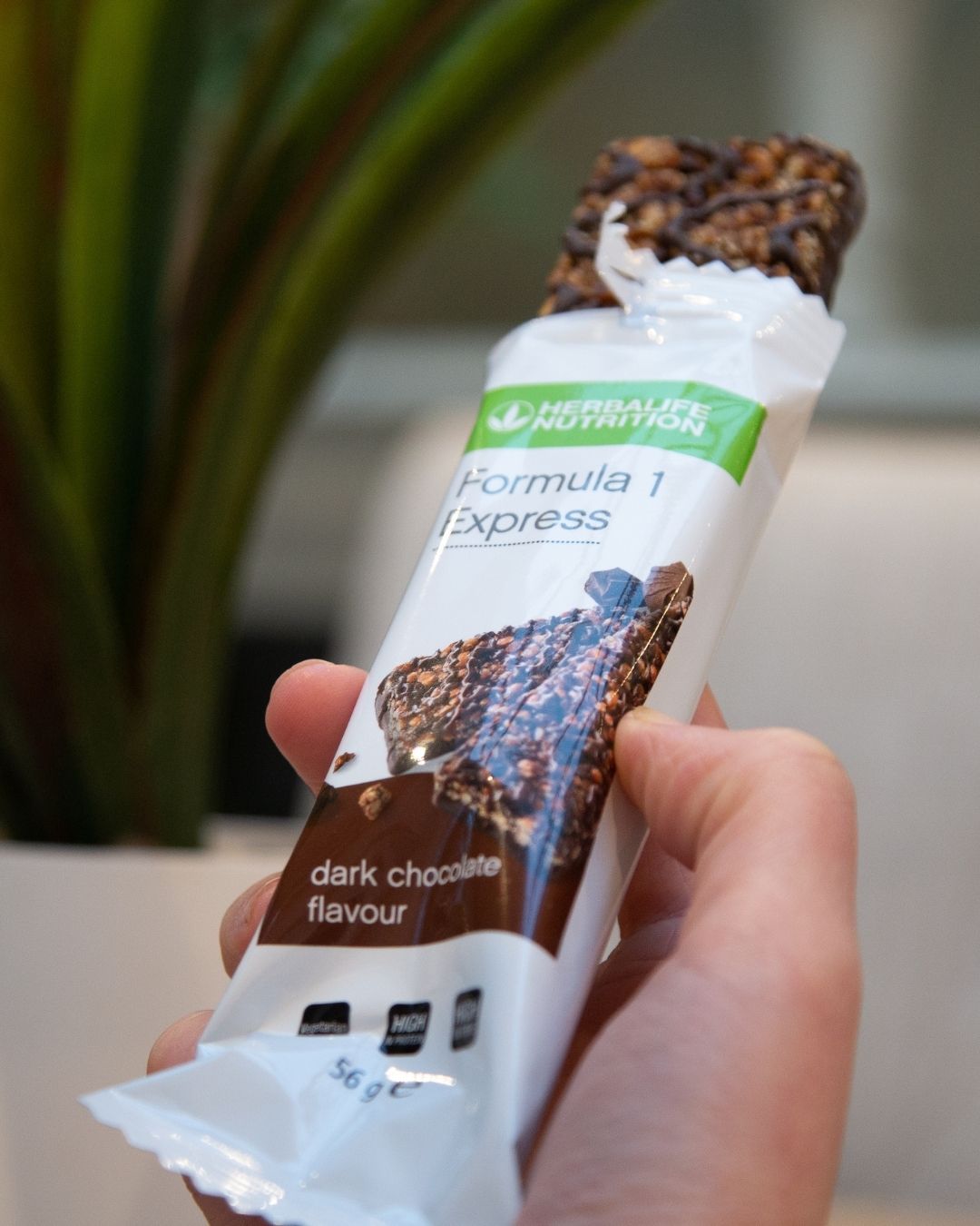 En Herbalife Formula 1 Expressbar halveis trukket ut av papiret sitt og en hånd som holder den. 