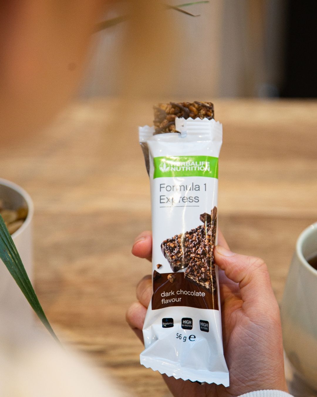 En Herbalife Formula 1 Expressbar halveis trukket ut av papiret sitt i ei hånd og en person som ser ned på den. 
