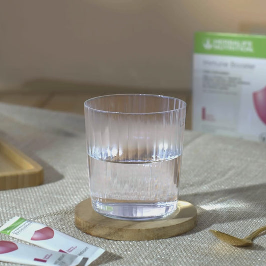 Video som viser en porsjonspose Immune Booster som helles i et glass vann, røres i med ei teskje og løftes opp for å drikkes. Videoen har teksten “Immune Booster. Formulated with EpiCor. A scientifically proven ingredient to help people live a healthier lifestyle by supporting immune and gut health. Order now”. 