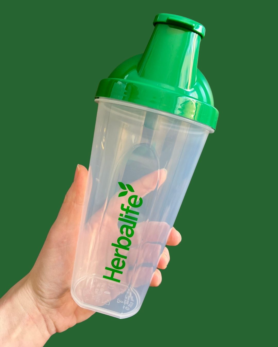 Shakerflaske med Herbalife-logo i handa på grønn bakgrunn fra Frokostshake.no.
