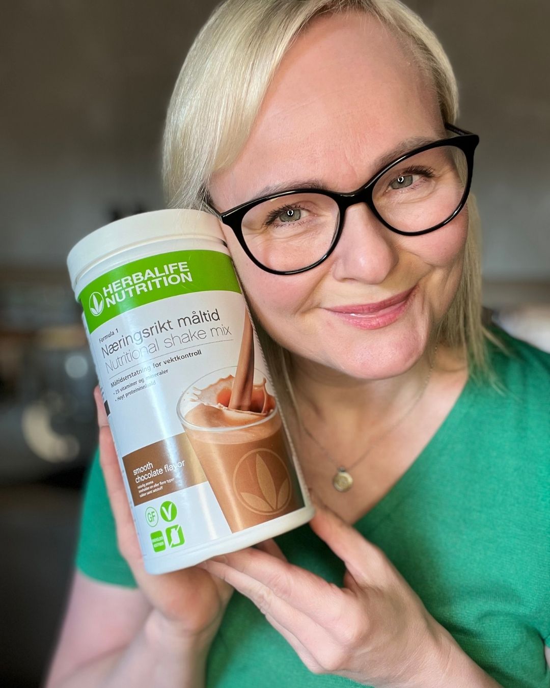 Helga holder en boks med Herbalife sjokoladeshake og smiler mot kamera